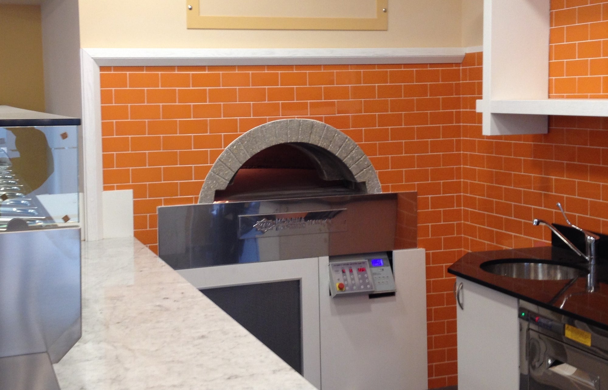 A milano fired oven enclosed by a orange brick wall design.